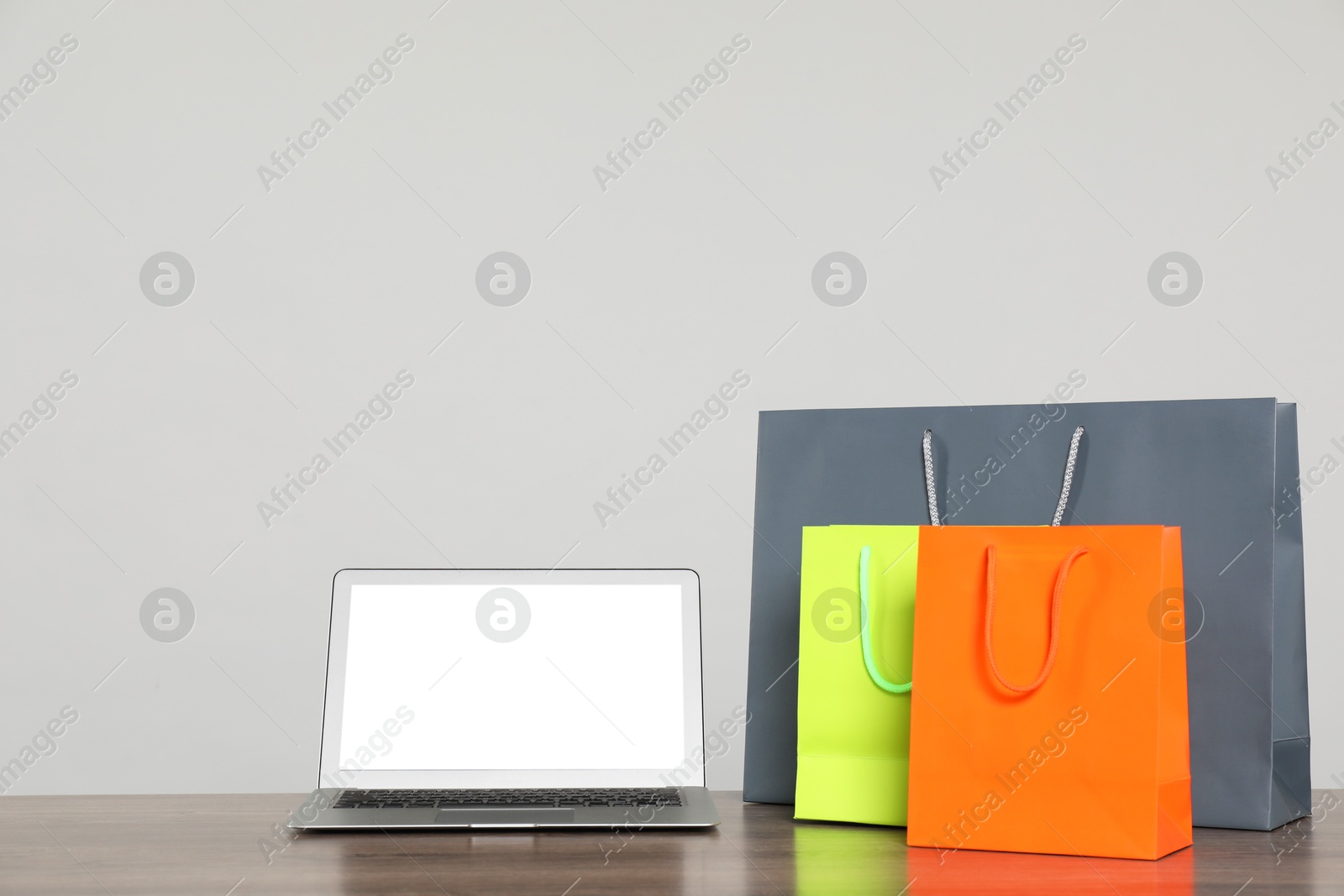 Photo of Internet shopping. Laptop and colorful paper bags on wooden table against grey background