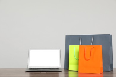 Photo of Internet shopping. Laptop and colorful paper bags on wooden table against grey background