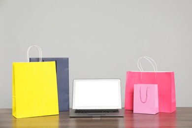 Photo of Internet shopping. Laptop and colorful paper bags on wooden table against grey background