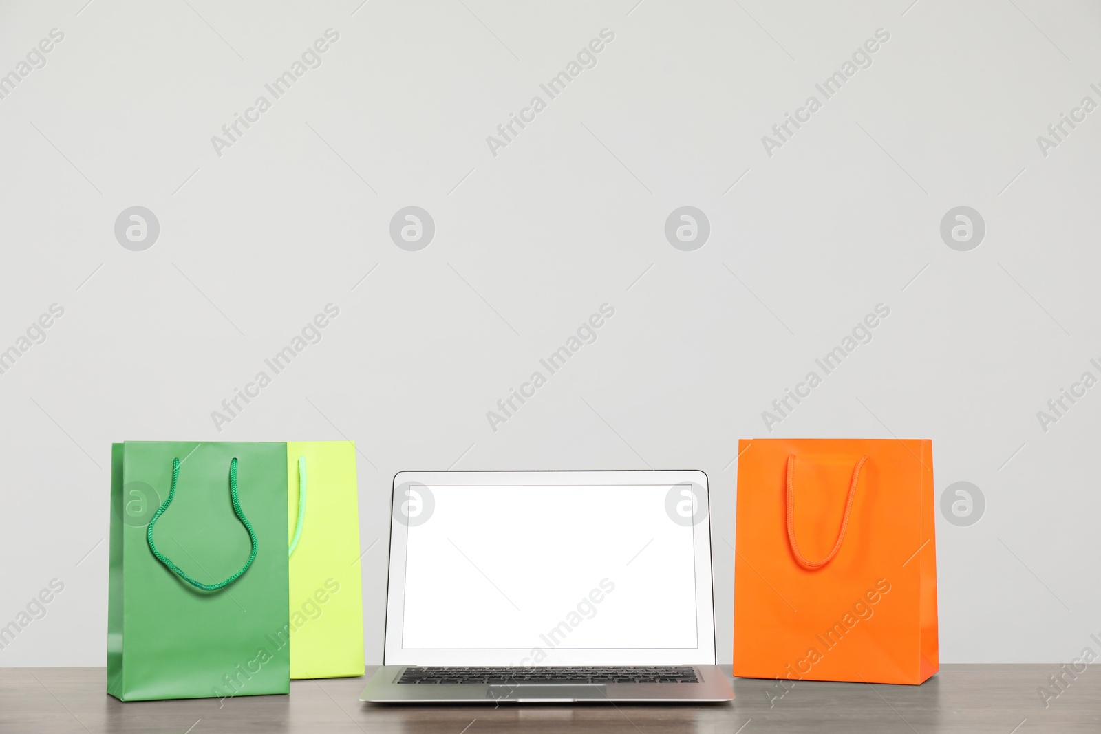 Photo of Internet shopping. Laptop and colorful paper bags on wooden table against grey background