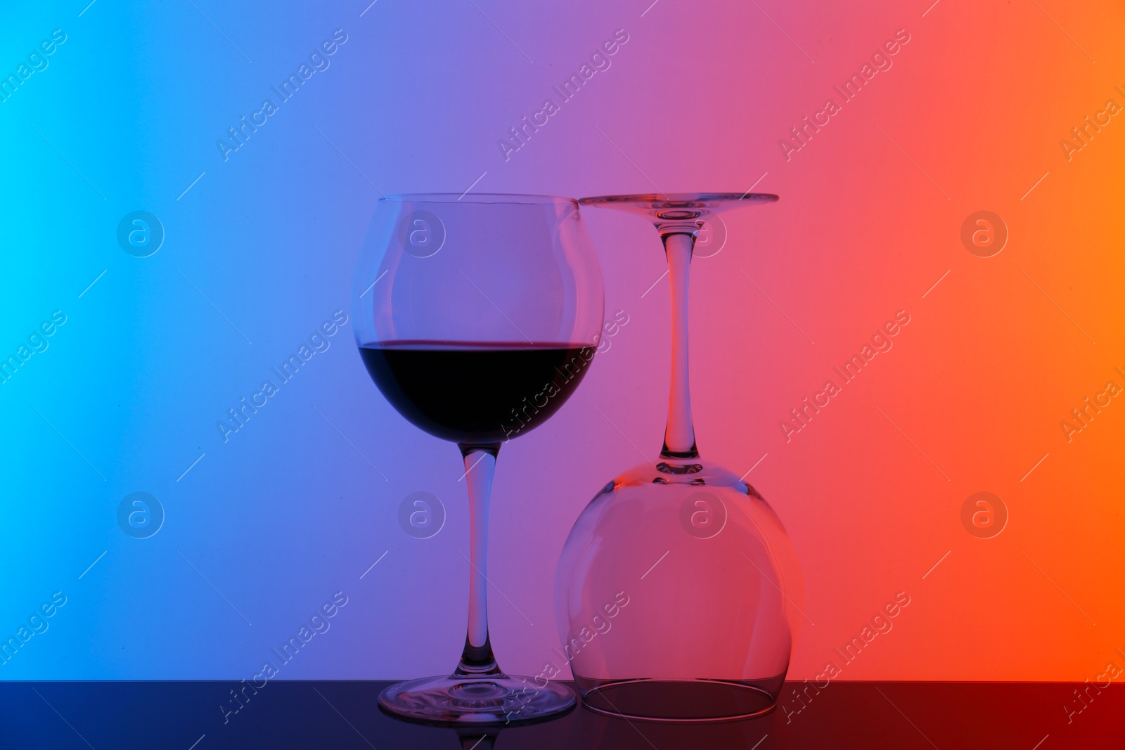 Photo of Glass of wine and empty one on table against color background