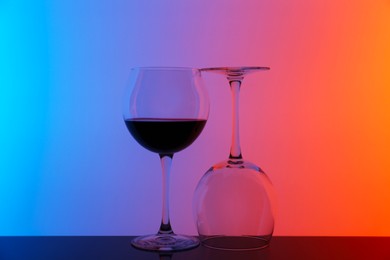 Photo of Glass of wine and empty one on table against color background