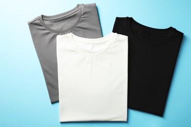 Photo of Blank t-shirts on light blue background, flat lay. Mockup for design