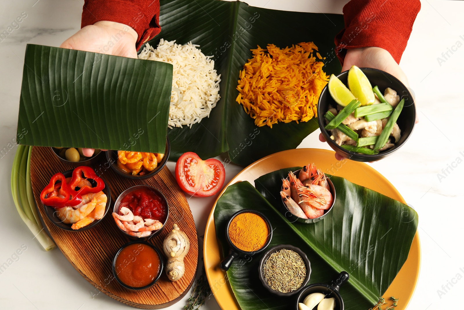 Photo of Woman holding piece of banana leaf and bowl with tasty food at white table, top view. Healthy eco serving