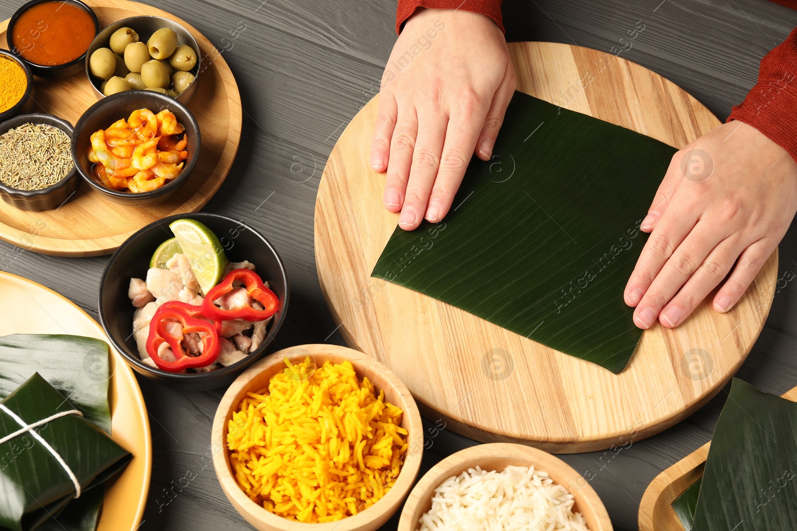 Photo of Woman with banana leaf at wooden table with different products, sauce and spices, top view. Healthy eco serving