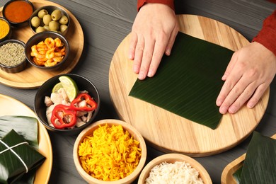 Woman with banana leaf at wooden table with different products, sauce and spices, top view. Healthy eco serving