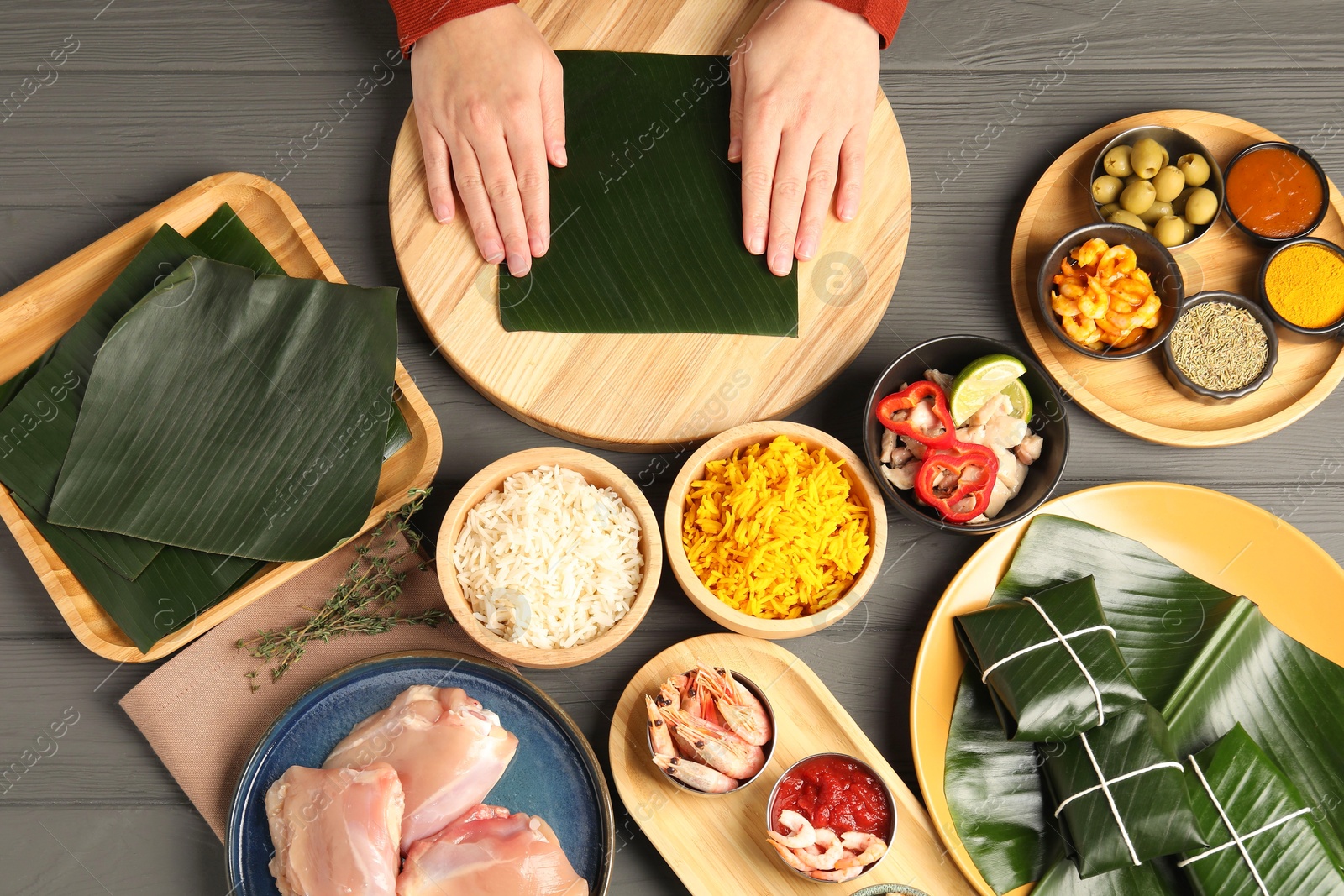 Photo of Woman with banana leaf at wooden table with different products, sauce and spices, top view. Healthy eco serving