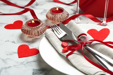 Photo of Romantic place setting for Valentine's day. Plate with cutlery, candles and decorative hearts on white marble table, closeup