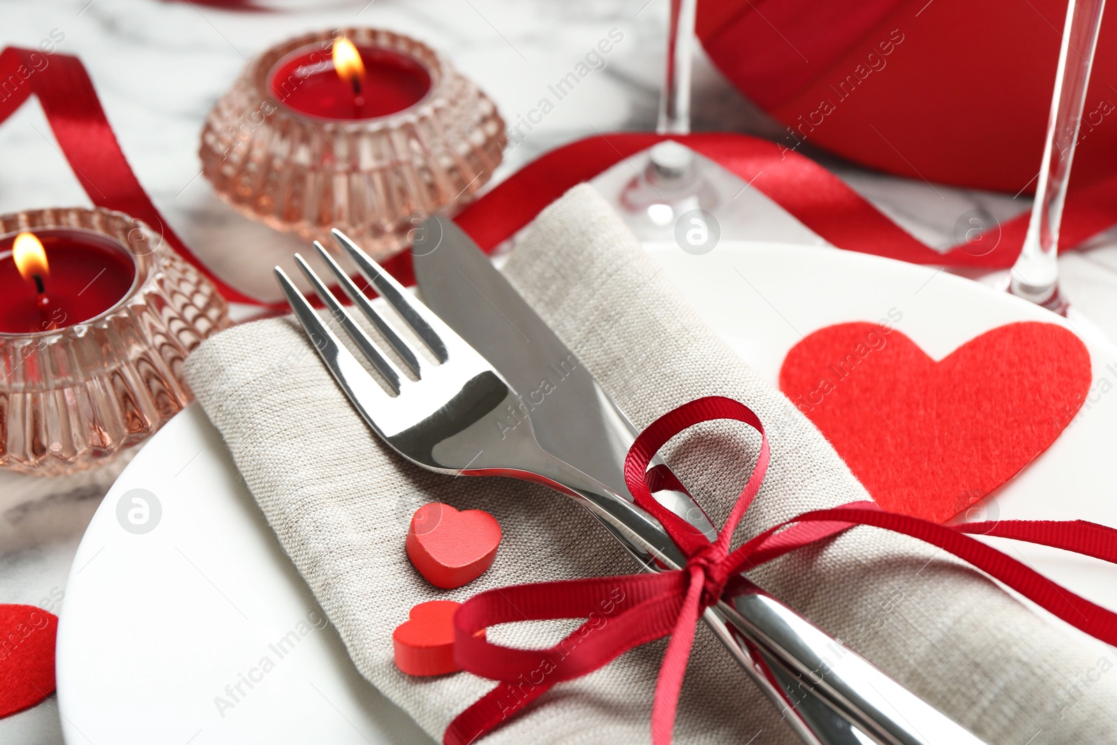 Photo of Romantic place setting for Valentine's day. Plate with cutlery, candles and decorative hearts on white table, closeup