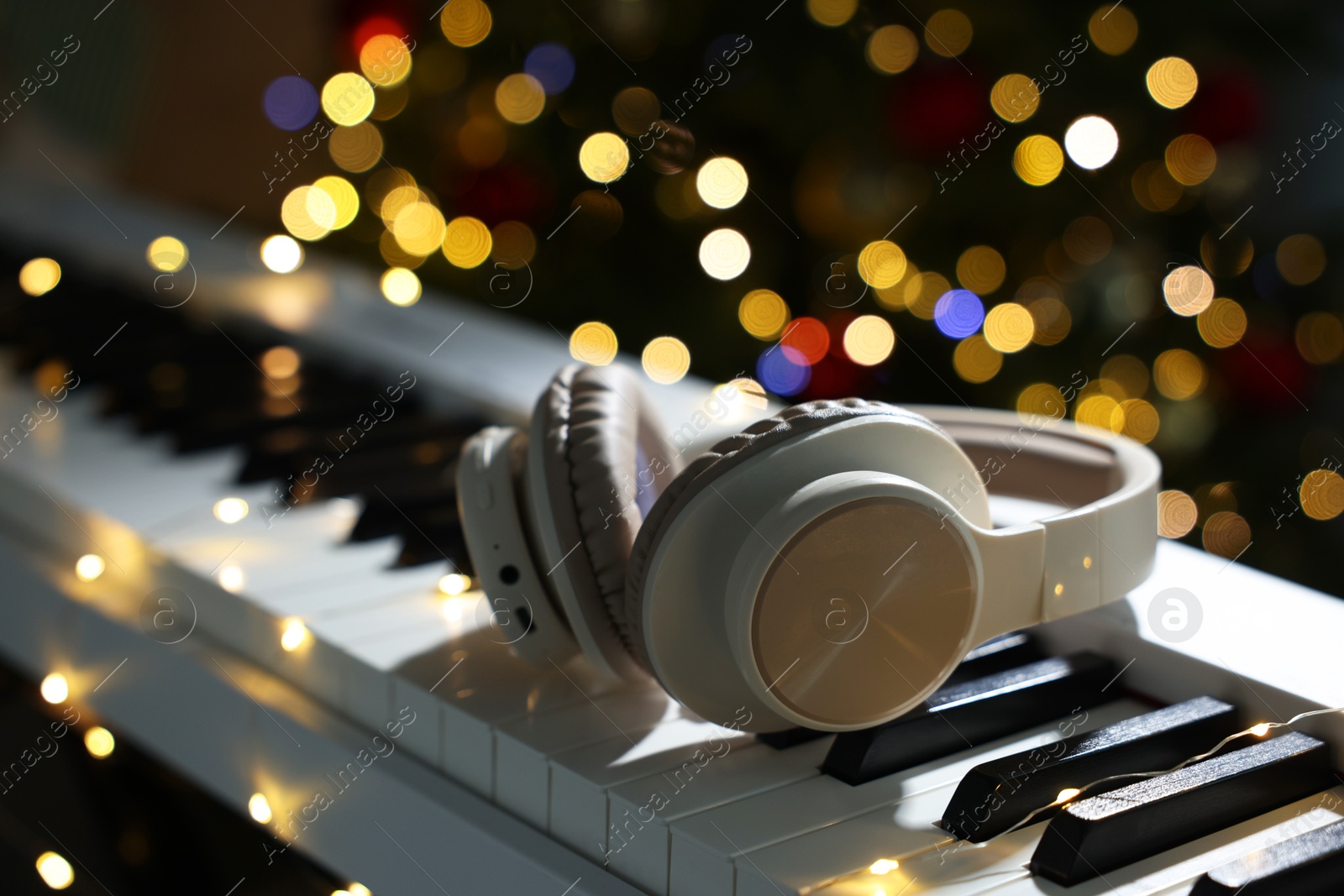 Photo of Headphones on electric piano against blurred lights, closeup. Bokeh effect