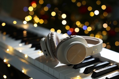 Photo of Headphones on electric piano against blurred lights, closeup. Bokeh effect