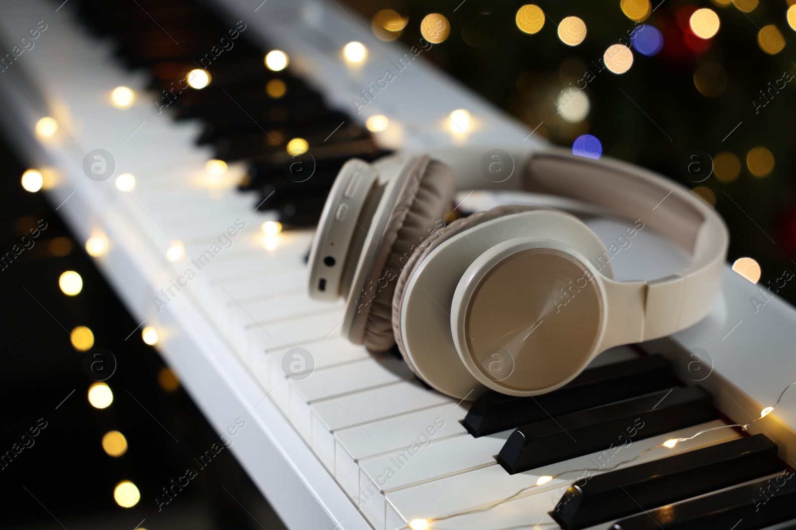 Photo of Headphones on electric piano against blurred lights, closeup. Bokeh effect