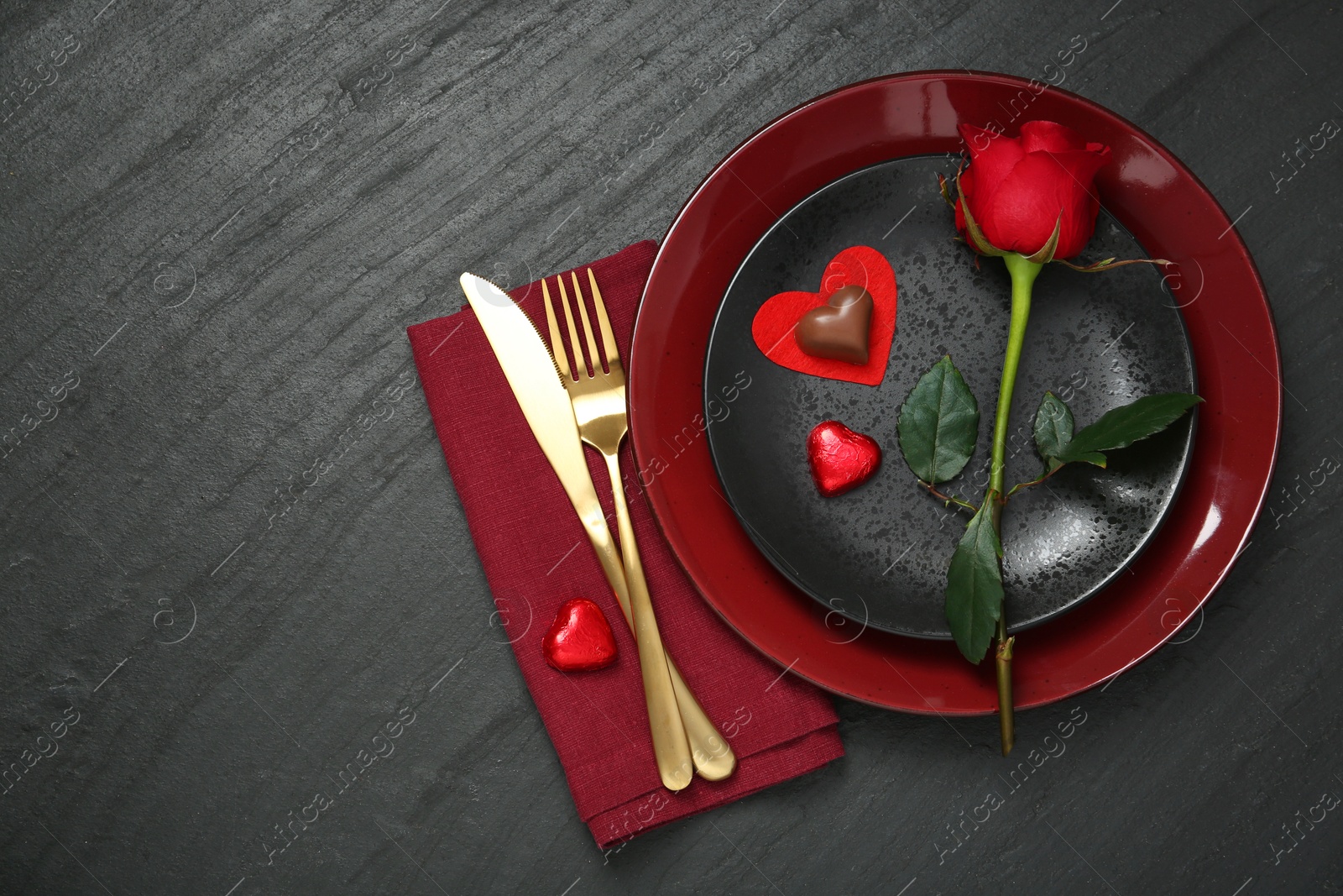 Photo of Romantic place setting with rose and plates on black table, top view. Valentine's day celebration