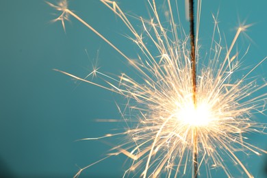 Photo of Bright burning sparkler on light blue background, closeup