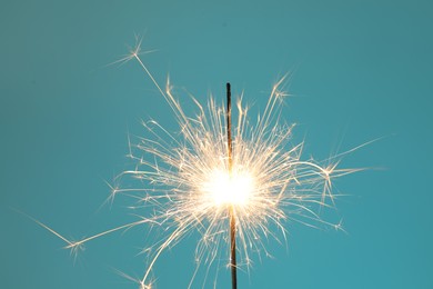 Photo of Bright burning sparkler on light blue background, closeup