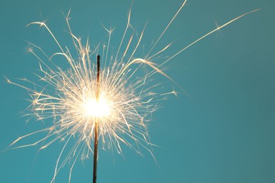 Photo of Bright burning sparkler on light blue background, closeup. Space for text