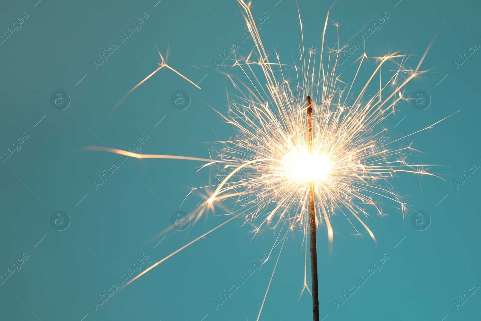 Photo of Bright burning sparkler on light blue background, closeup. Space for text