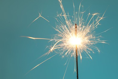 Photo of Bright burning sparkler on light blue background, closeup. Space for text