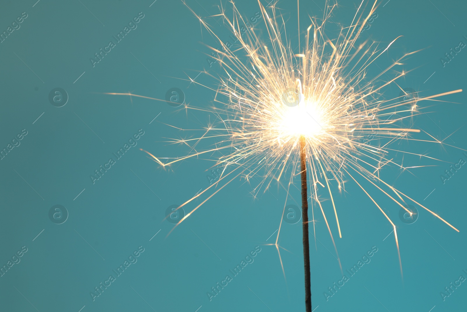 Photo of Bright burning sparkler on light blue background, closeup. Space for text