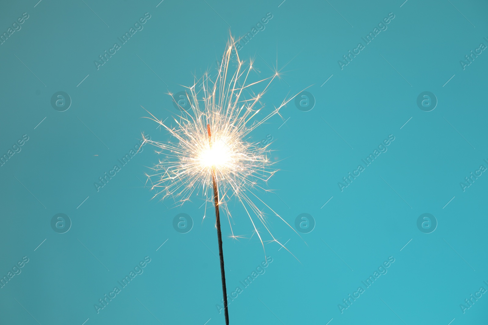 Photo of Bright burning sparkler on light blue background, closeup