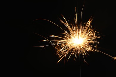 Photo of Bright burning sparkler on black background, closeup. Space for text