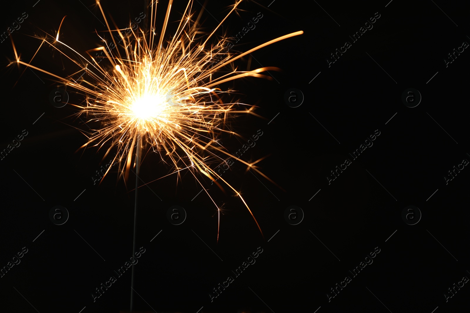 Photo of Bright burning sparkler on black background, closeup. Space for text