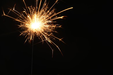 Photo of Bright burning sparkler on black background, closeup. Space for text