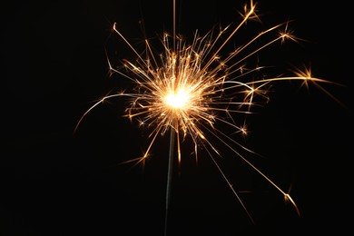 Photo of Bright burning sparkler on black background, closeup