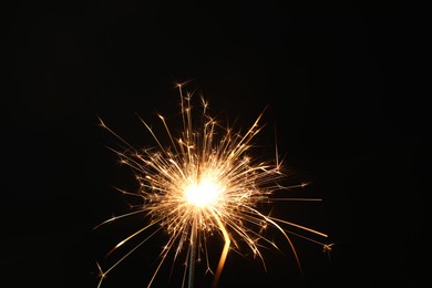 Photo of Bright burning sparkler on black background, closeup