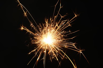 Photo of Bright burning sparkler on black background, closeup