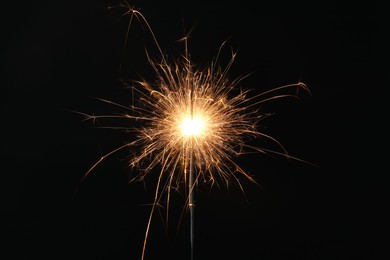 Photo of Bright burning sparkler on black background, closeup