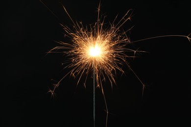 Photo of Bright burning sparkler on black background, closeup