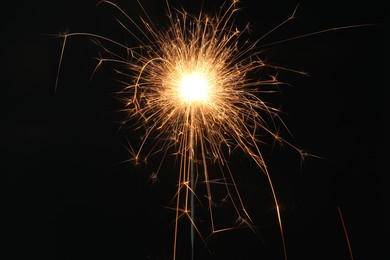 Photo of Bright burning sparkler on black background, closeup