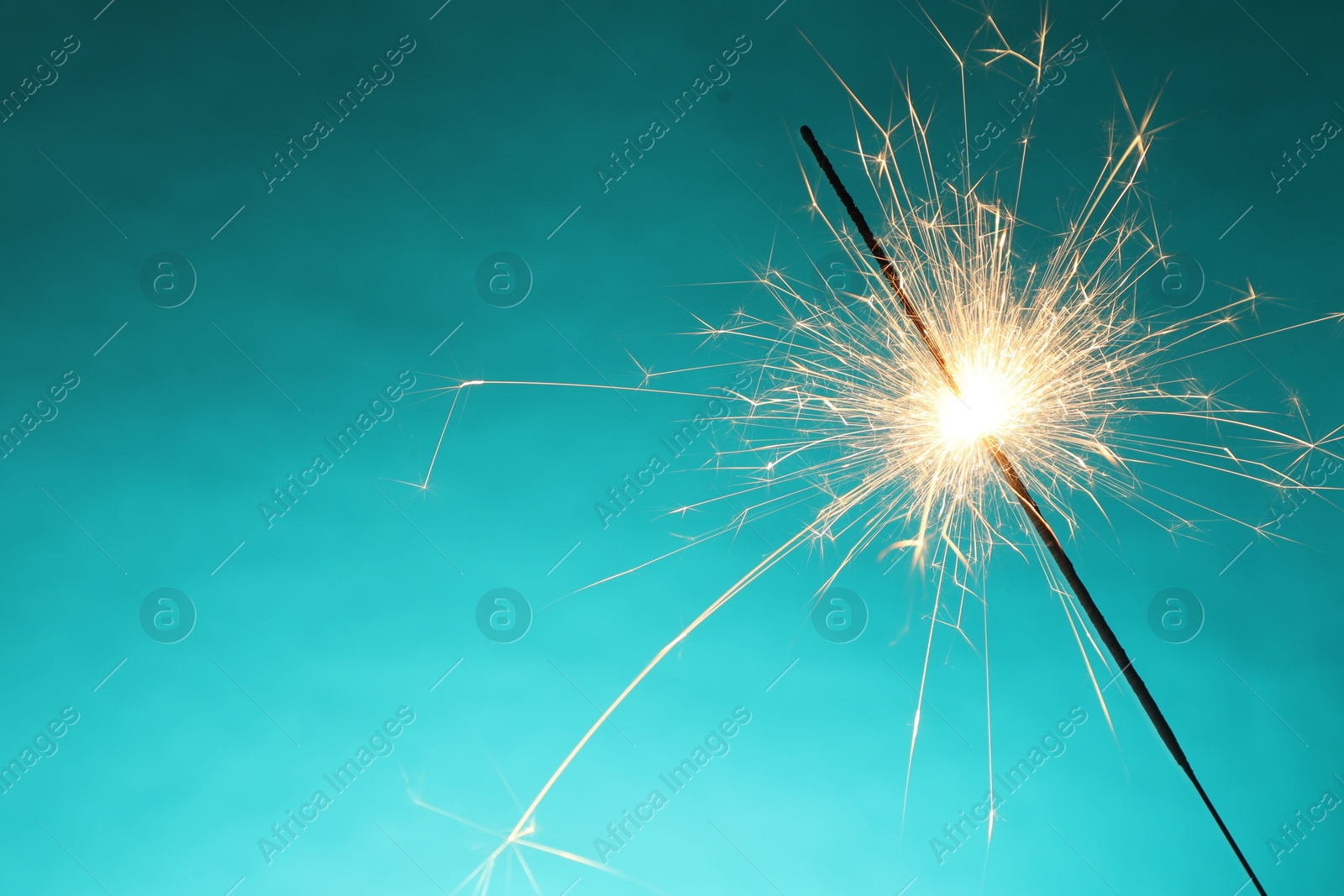 Photo of Bright burning sparkler on turquoise background, closeup. Space for text