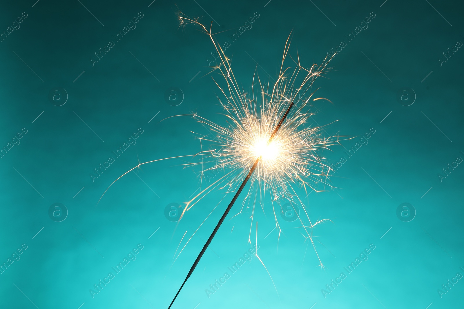 Photo of Bright burning sparkler on turquoise background, closeup