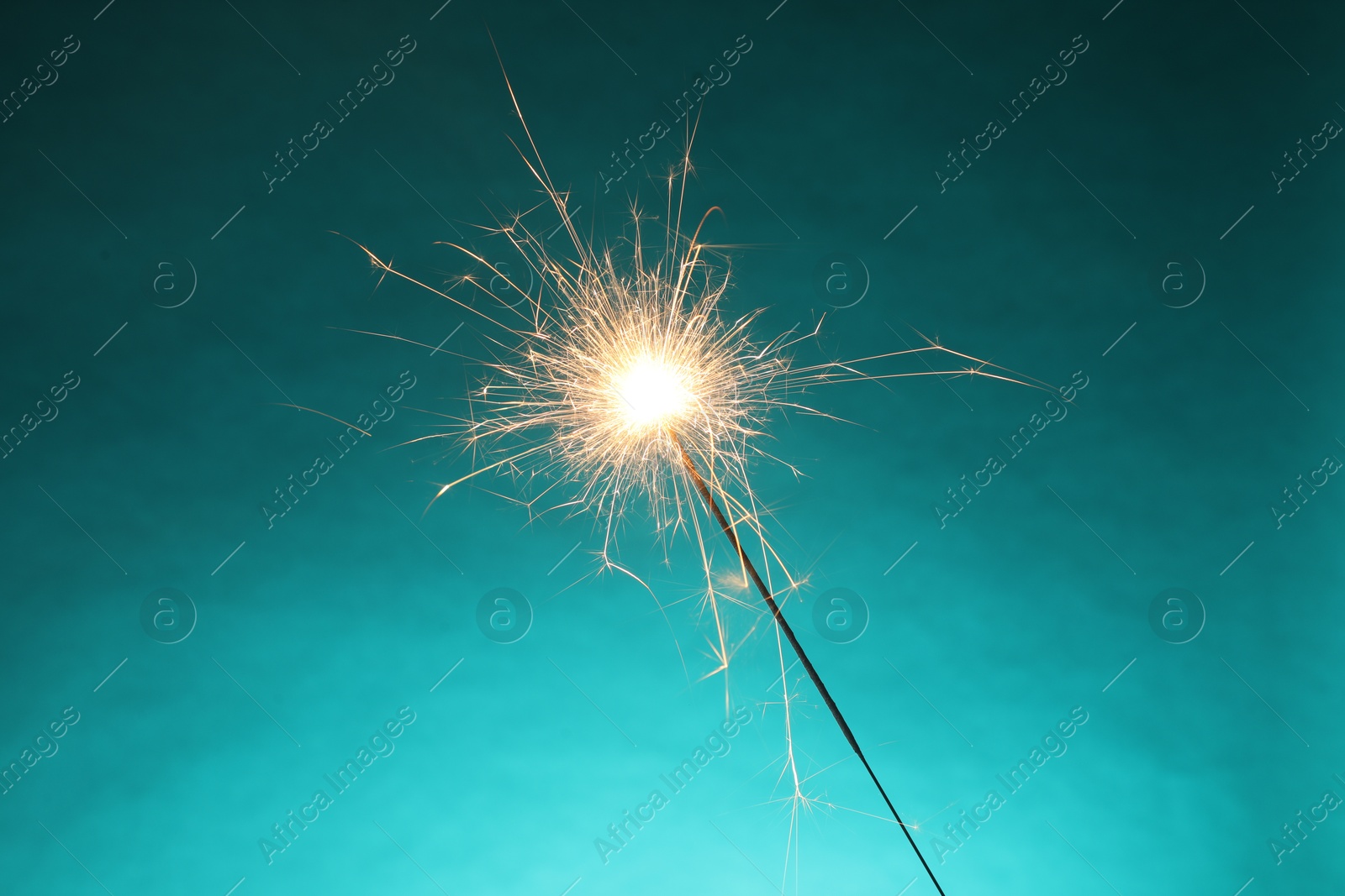 Photo of Bright burning sparkler on turquoise background, closeup