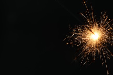 Photo of Bright burning sparkler on black background, closeup. Space for text