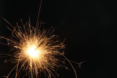 Photo of Bright burning sparkler on black background, closeup. Space for text