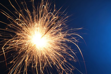 Photo of Bright burning sparkler on blue background, closeup