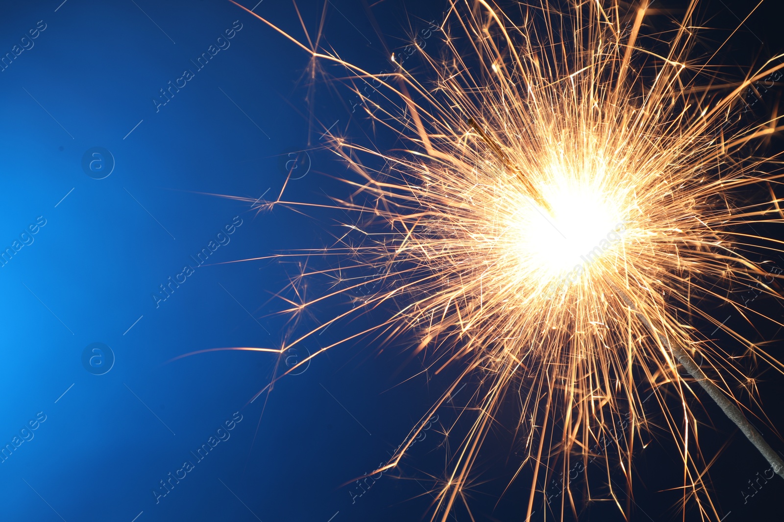 Photo of Bright burning sparkler on blue background, closeup. Space for text