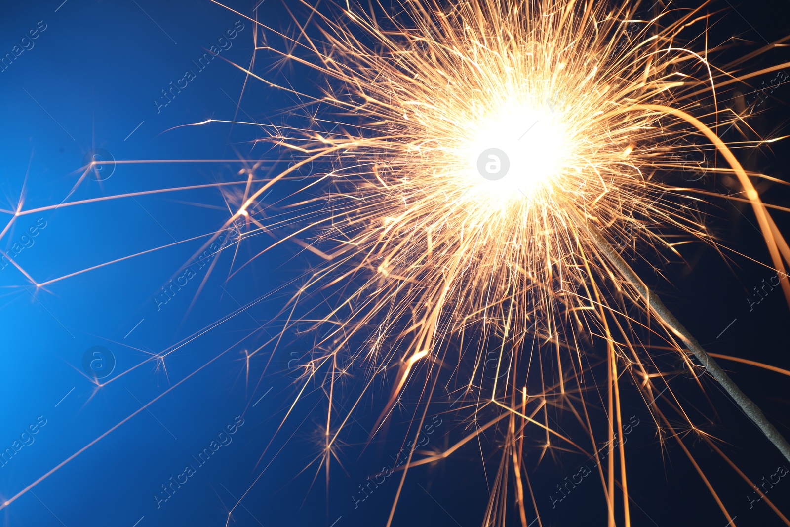 Photo of Bright burning sparkler on blue background, closeup