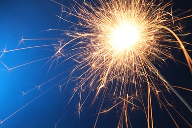 Photo of Bright burning sparkler on blue background, closeup