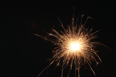 Photo of Bright burning sparkler on black background, closeup. Space for text