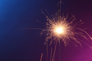 Photo of Bright burning sparkler in color lights, closeup. Space for text