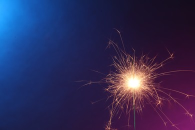 Photo of Bright burning sparkler in color lights, closeup. Space for text