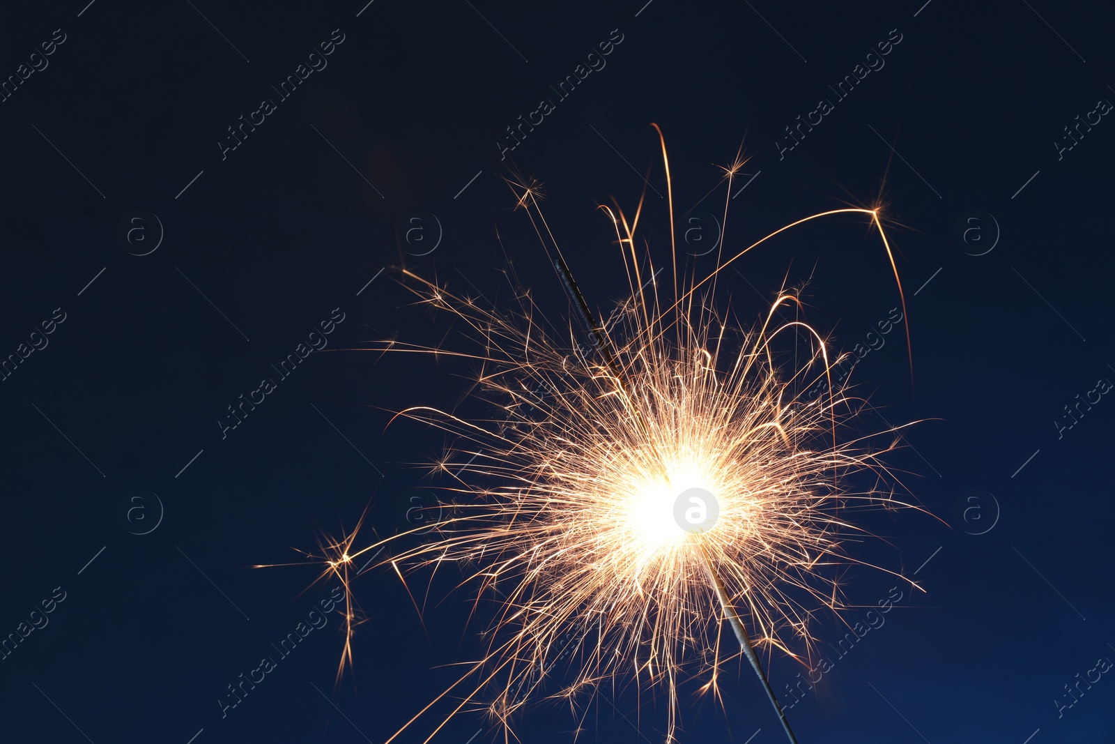 Photo of Bright burning sparkler on dark blue background, closeup