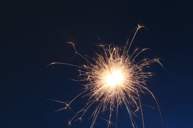 Photo of Bright burning sparkler on dark blue background, closeup