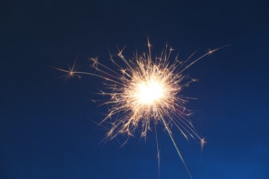 Photo of Bright burning sparkler on dark blue background, closeup