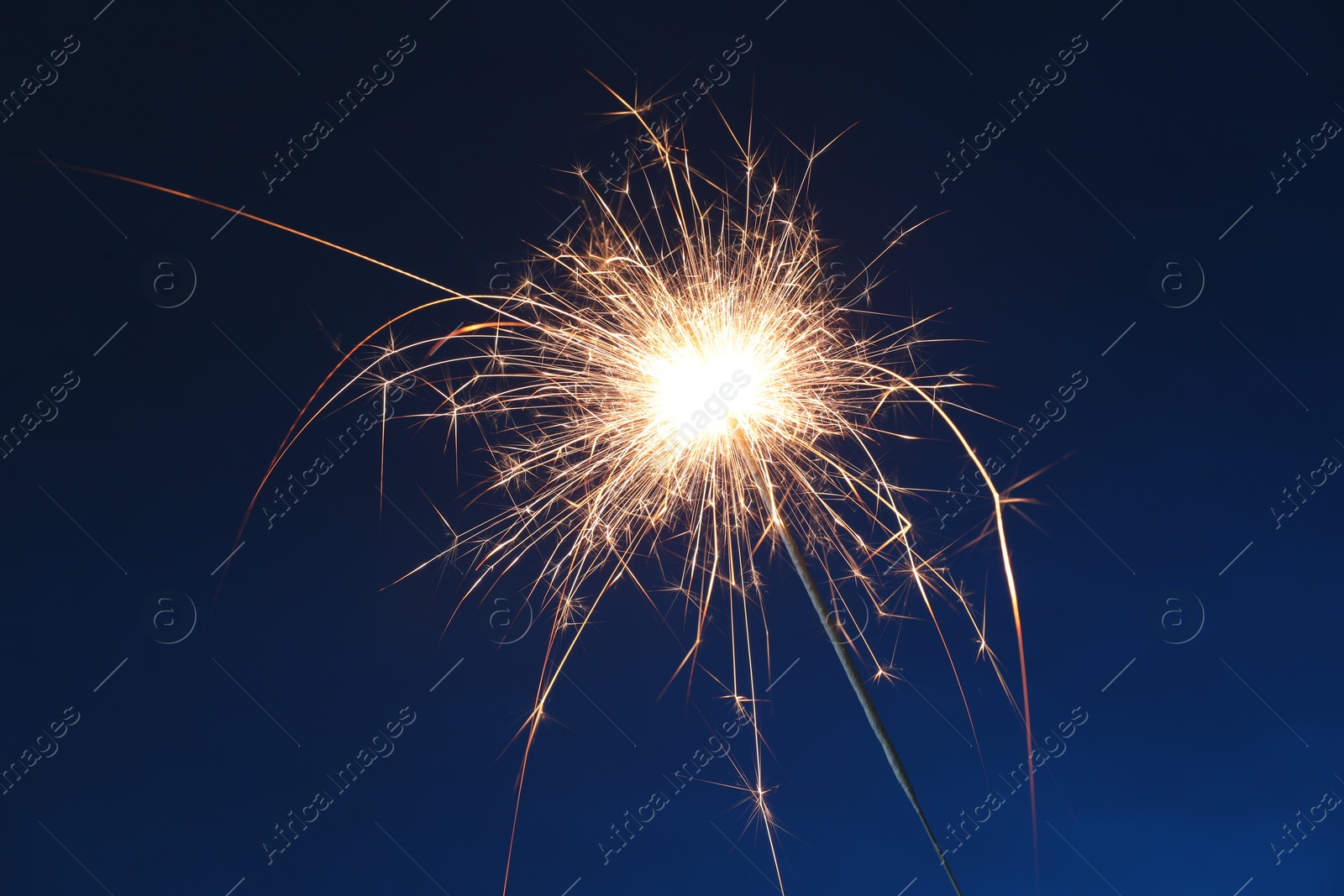 Photo of Bright burning sparkler on dark blue background, closeup