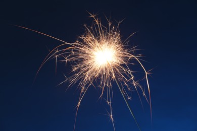 Photo of Bright burning sparkler on dark blue background, closeup